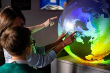 Delivering impact to the next generation at Winchester Science Centre Big Bang Event (February 2020). Scientists describe colourful models of the ocean on a 3D globe to a busy room of school children. [cc]
