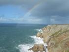 A rainbow is created from the storm waves crashing against a high cliff